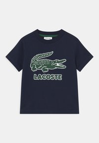 Mörkblå bomull t-shirt med en grön krokodil-logotyp och "LACOSTE" i upphöjd text. Kort ärm och rund halsringning.