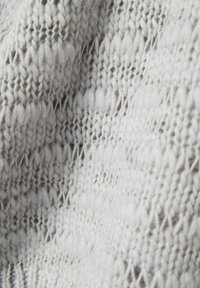 Világosszürke kötött anyag, amely változatos textúrával rendelkezik, szoros és laza öltések keverékét mutatja meg geometrikus mintázatban.