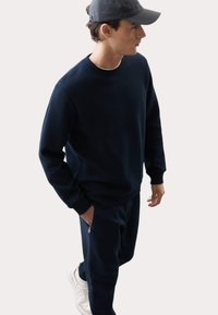 Sudadera azul marino con un patrón de espiga, de mangas largas, puños acanalados, combinada con pantalones a juego y zapatillas blancas.