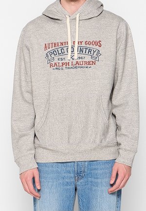 Felpa con cappuccio grigio chiaro con tasca frontale, coulisse e logo testuale "Polo Country Ralph Lauren" in rosso e blu, indossata con jeans blu.