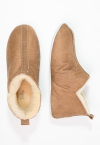 Chaussons en suède brun avec un intérieur en crème doux, design à enfiler, détails de couture sur le côté et semelle en caoutchouc blanc.