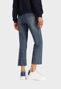 Jeans in denim blu accorciati con taglio dritto, dotati di tasche posteriori e orlo cucito, abbinati a sneakers bianche e blu.
