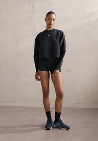 Black cropped sweatshirt with a small white Nike logo, paired with black shorts and blue athletic shoes. Smooth fabric, minimalistic design.