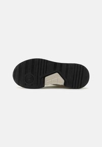 Suela de zapato de goma negra con ranuras texturizadas, patrón circular cerca del tacón y una sección beige insertada para mayor agarre.