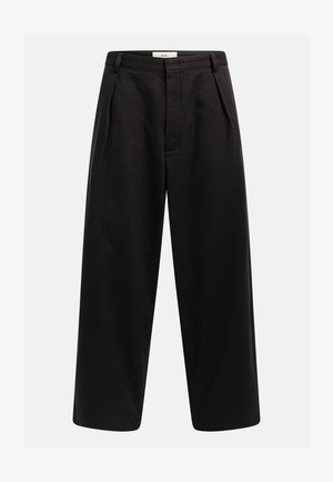 Pantaloni neri a gamba larga con pieghe frontali, passanti per cintura e chiusura nascosta, etichettati "Rebel" sulla vita.