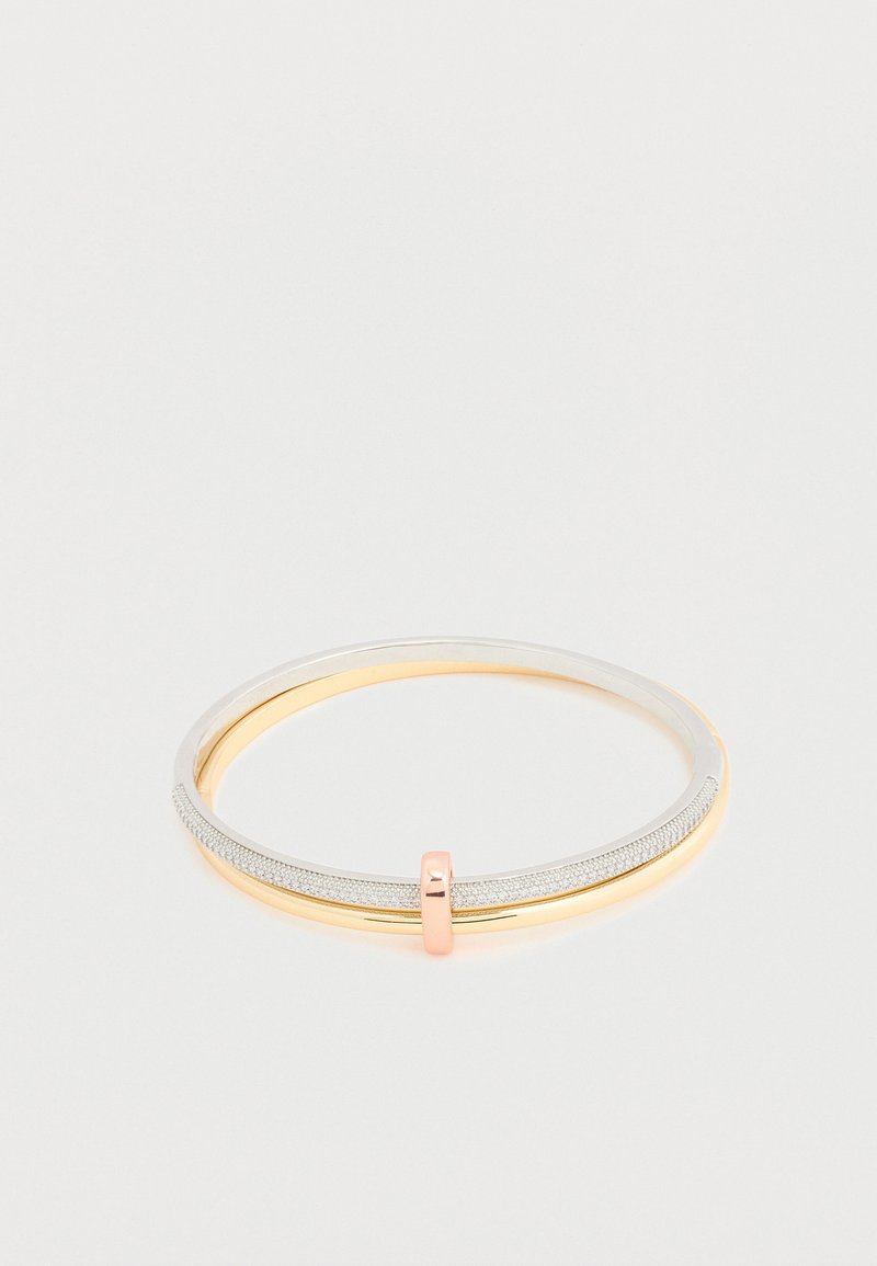 Bracelet double jonc avec un bracelet argenté pailleté et un bracelet doré, reliés par un petit fermoir en or rose sur fond blanc.