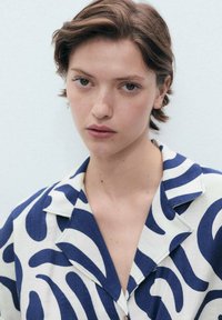 A collared shirt featuring a blue and white abstract wave pattern, made from lightweight fabric, with a button closure and relaxed fit.