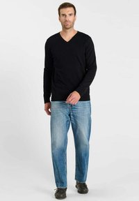 Zwarte lange mouwen v-hals trui, gecombineerd met lichtblauwe rechte jeans en zwarte schoenen, wat een casual outfit vormt. Eenvoudig ontwerp, geen patronen.