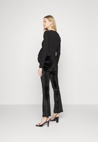 Blusa preta de manga longa combinada com calças pretas brilhantes e largas. O conjunto apresenta uma silhueta ajustada e sandálias de salto alto.