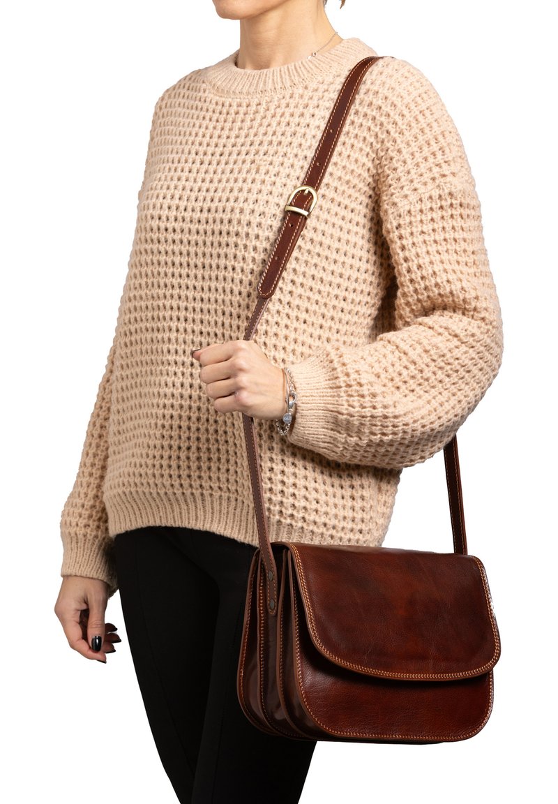 Borsa a tracolla in pelle marrone con chiusura a pattina, caratterizzata da un bordo cucito in contrasto e una tracolla regolabile. Maglione beige a maglia con texture.
