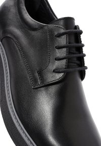 Zwarte leren schoen met een gladde afwerking, vetersluiting en ronde neus. Bevat een grijze rubberen zool en minimale stikseldetails.