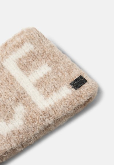 Tissu en laine tricoté beige et blanc avec une grande lettre "E" et une petite étiquette rectangulaire noire attachée dans le coin.