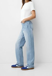 Light blue wide-leg jeans paired with a fitted white t-shirt and blue sneakers with white accents and beige soles. Soft denim texture.