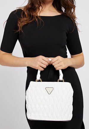 Femme en robe noire tenant un sac à main matelassé blanc avec des ferrures dorées et un logo triangulaire à l’avant.