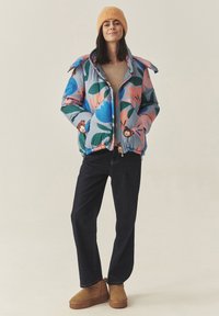 Farverig pufferjakke med blomster mønstre i blå, pink og grøn. Strikket beige sweater og mørkeblå jeans. Brune støvler med blød sål.