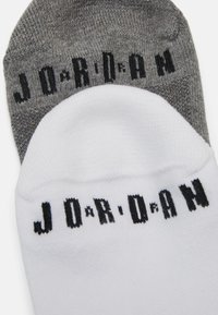Dos pares de calcetines de tripulación, uno blanco y otro gris. Ambos presentan la inscripción en negro "J O R D A N" en la parte superior. Material de punto texturizado.