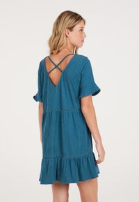 Teal, lyhythihainen mekko, jossa on hihansuiden röyhelö, avonainen selkä ristiin menevillä hihnoilla ja pitsikoristeet vyötäröllä. Pehmeä, kevyt kangas.