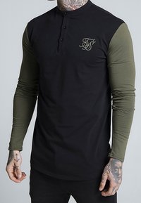 Black long-sleeve henley shirt with olive green sleeves, featuring a crew neck, three black buttons, and a gold logo detail on the chest.