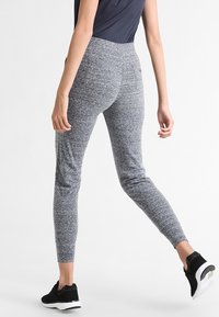 Šedé texturované legíny s vysokým pasem a bočními kapsami, spárované s černými sportovními botami. Navrženo pro pohodlí a flexibilitu.