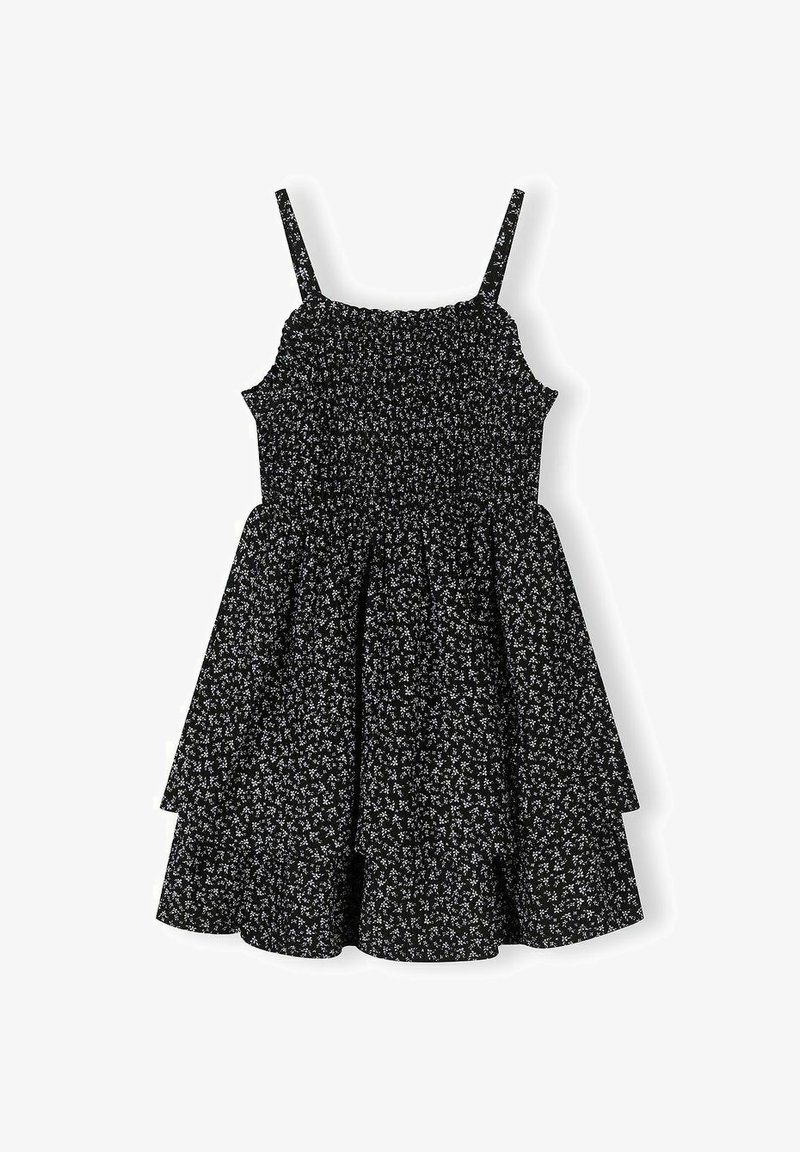Robe noire sans manches avec bretelles fines, corsage froncé, jupe évasée à volants et petit motif floral blanc.