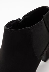 Černá kotníková bota vyrobená z jemného semiše a elastické tkaniny, se zaoblenou špičkou, nízkým podpatkem a zipovým uzávěrem pro snadné obouvání.