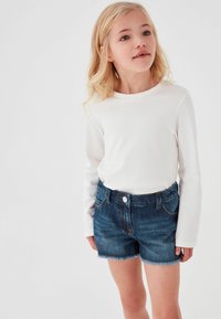 Vit långärmad topp som kombineras med mörka denimshorts med fransar i kanten. Shortsen har knappstängning och fickor.