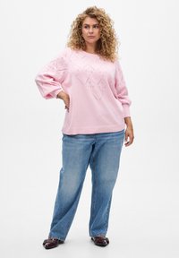 Roze gebreide trui met een ruitpatroon, lange mouwen en geribbelde zoom, gecombineerd met lichtblauwe losse jeans en donkerpaarse schoenen.