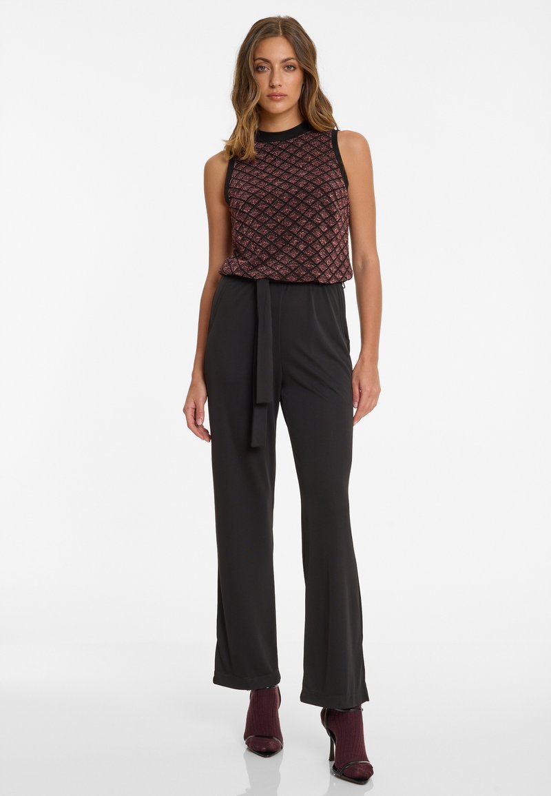 Zwarte jumpsuit met een aansluitende taille en wijde benen, gecombineerd met een mouwloze, gebloemde top met een diamanten patroon in tinten van rood en zwart.