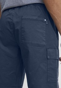 Shorts cargo de culoare bleumarin, confecționate dintr-un material ușor, având un buzunar pe spate și un finisaj texturat. Talie elastică cu un branding subtil.