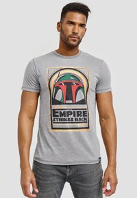 Grå bomulds t-shirt med et farverigt grafik af Boba Fetts hjelm med teksten "The Empire Strikes Back" under. Korte ærmer, rund hals.