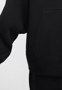 Sort sweatshirt med rund halsudskæring, sænkede skuldre og en frontlomme. Glat struktur og syningsdetaljer langs kanten.
