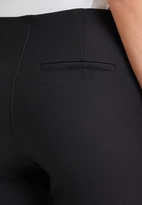 Czarne spodni z wysokim stanem o gładkiej fakturze, z małą kieszenią z tyłu i subtelnymi detalami stębnowania.
