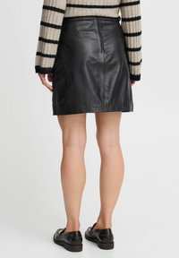 Minifalda de cuero negra con forma ajustada, que cuenta con un cierre trasero y una textura suave. Combinada con un suéter a rayas y mocasines negros.
