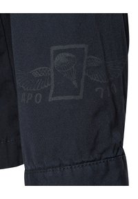 Zbliżenie na ciemny materiał, na którym widać subtelny grafikę przedstawiającą rękę trzymającą kulę w prostokątnym konturze i częściowy tekst poniżej.