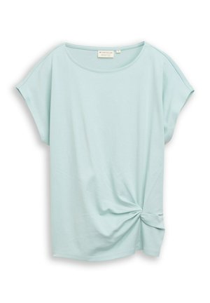 Blouse bleu clair à manches courtes avec un col rond et un détail noué torsadé sur le bas du côté droit.