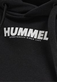 Felpa nera in cotone, con un grande logo bianco "HUMMEL" e il testo "SPORTSWEAR SINCE 1923" sotto. Visibili i cordini del cappuccio.