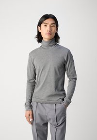 Pilkas polo megztinis, pagamintas iš lygios, švelnios medžiagos, su ilgomis rankovėmis ir prigludusia forma. Suderintas su dryžuotomis kelnėmis.
