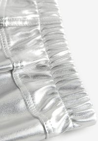 Metallisches Silbergewebe zeigt ein gerafftes Design entlang des Randes und besticht durch eine glatte Textur mit sichtbaren Nähten.