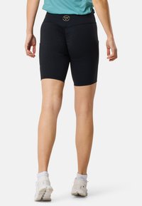 Pantaloni ciclistici neri con vita alta, texture liscia e tasche laterali. Presentano un piccolo logo sul retro. Indossati con scarpe sportive bianche.