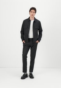 Dark gray jacket with button closure and two chest pockets, paired with matching trousers and black shoes. Simple design, smooth fabric.