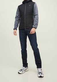 Lightweight, hooded jacket featuring a quilted black front and gray sleeves. Paired with dark jeans and athletic shoes.