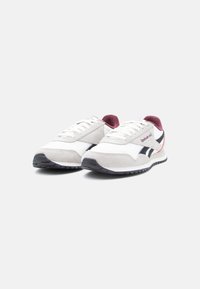 Par bijelih i sivih Reebok tenisica s crnim prugama i bordo unutrašnjošću, prikazanih pod kutom na bijeloj pozadini.