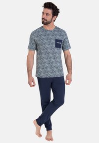 Ensemble de pyjama pour homme composé d'une chemise à manches courtes verte à motifs avec une poche poitrine et un pantalon à taille élastique bleu marine. Tissu doux.