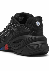 Chaussure de sport noire avec empeigne en mesh et synthétique, dotée d'accents réfléchissants, d'un talon arrondi et d'un design rouge et bleu sur la semelle extérieure.