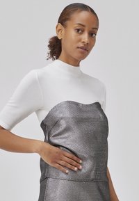 Hvid ribbet top med høj krave, parret med en metallic sølvfarvet struktureret kjole med en bølget halsudskæring og tætsiddende silhuet.