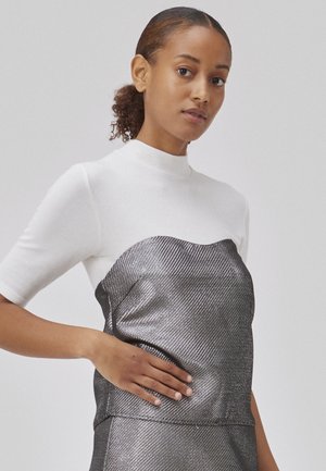 White ribbed top with a high collar, paired with a metallic silver textured dress featuring a wavy neckline and fitted silhouette.