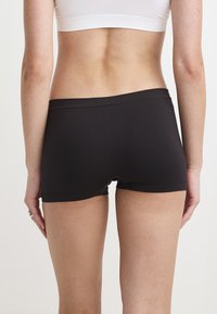 Schwarze Baumwollshorts mit einem elastischen Bund, die eine glatte Textur und ein figurnahes Design aufweisen, von hinten betrachtet.