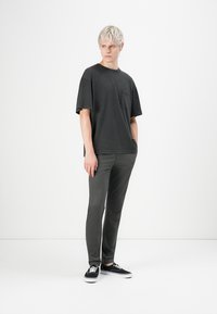 Dark gray cotton T-shirt with short sleeves and a chest pocket, paired with matching dark gray slim-fit pants and black sneakers.