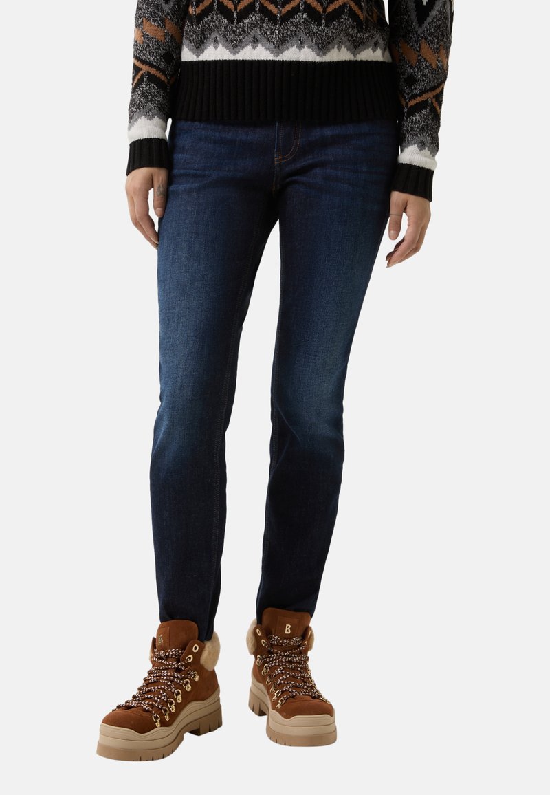Tmavě modré úzké džíny v kombinaci s hnědými šněrovacími botami s kožešinovými akcenty a silnou podešví, nošeny s vzorovaným svetr.