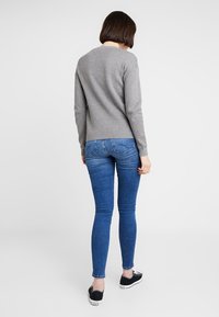 Gray sweater with a round neckline, paired with blue skinny jeans and black sneakers. The fabric appears soft with a smooth texture.